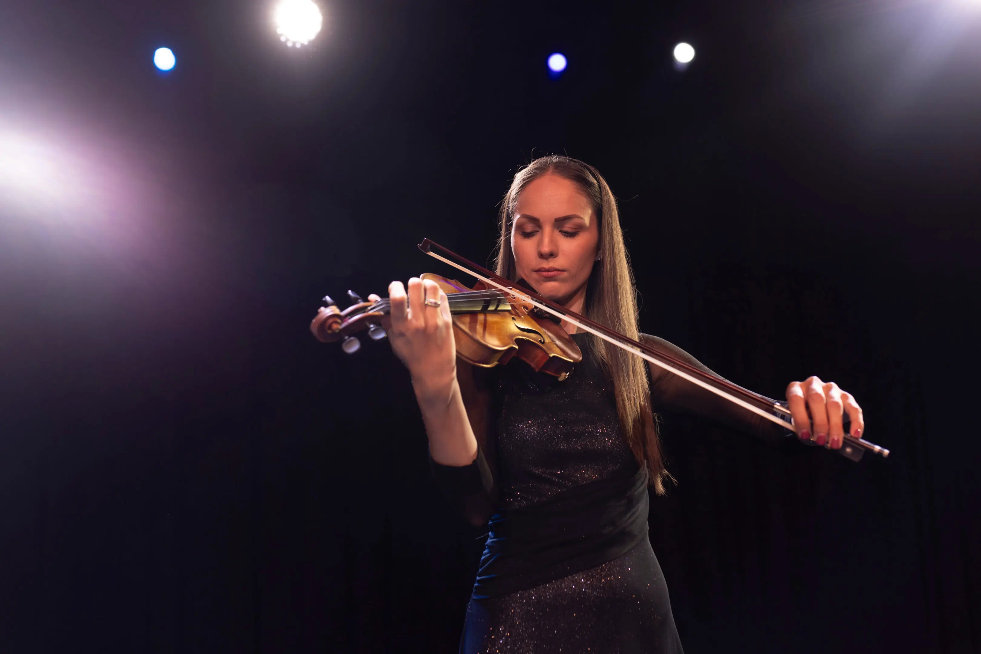 Violinist performing on stage under lights.