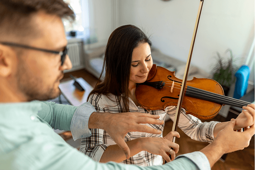 Two people playing violin together in a cozy room.