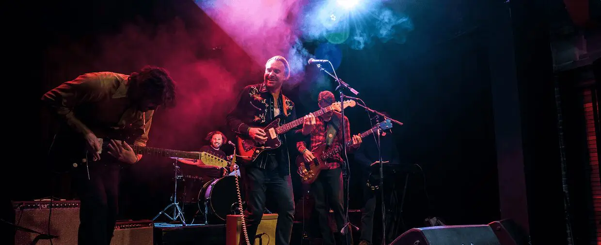 Band performing live on stage with colorful lighting and smoke effects.