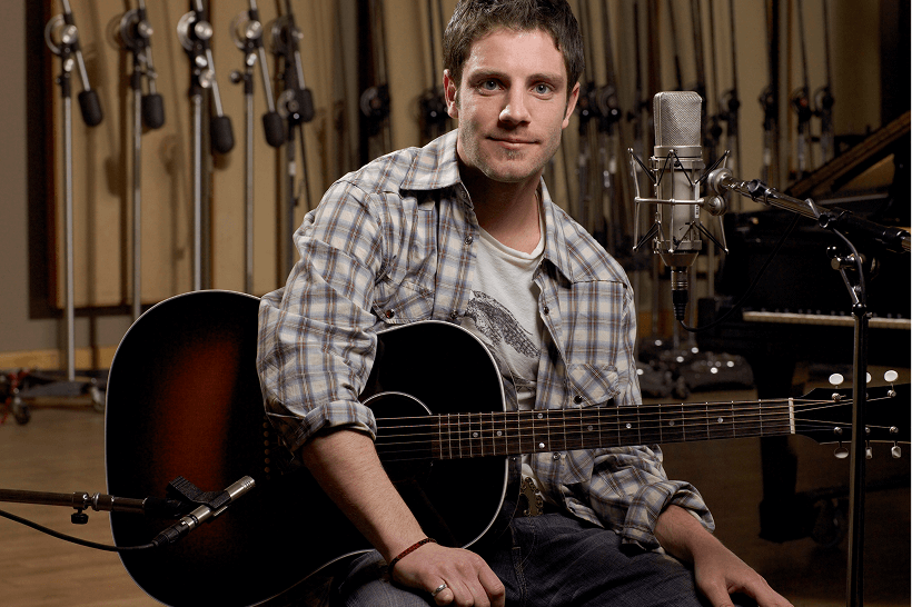 Man sitting with an acoustic guitar in a recording studio.