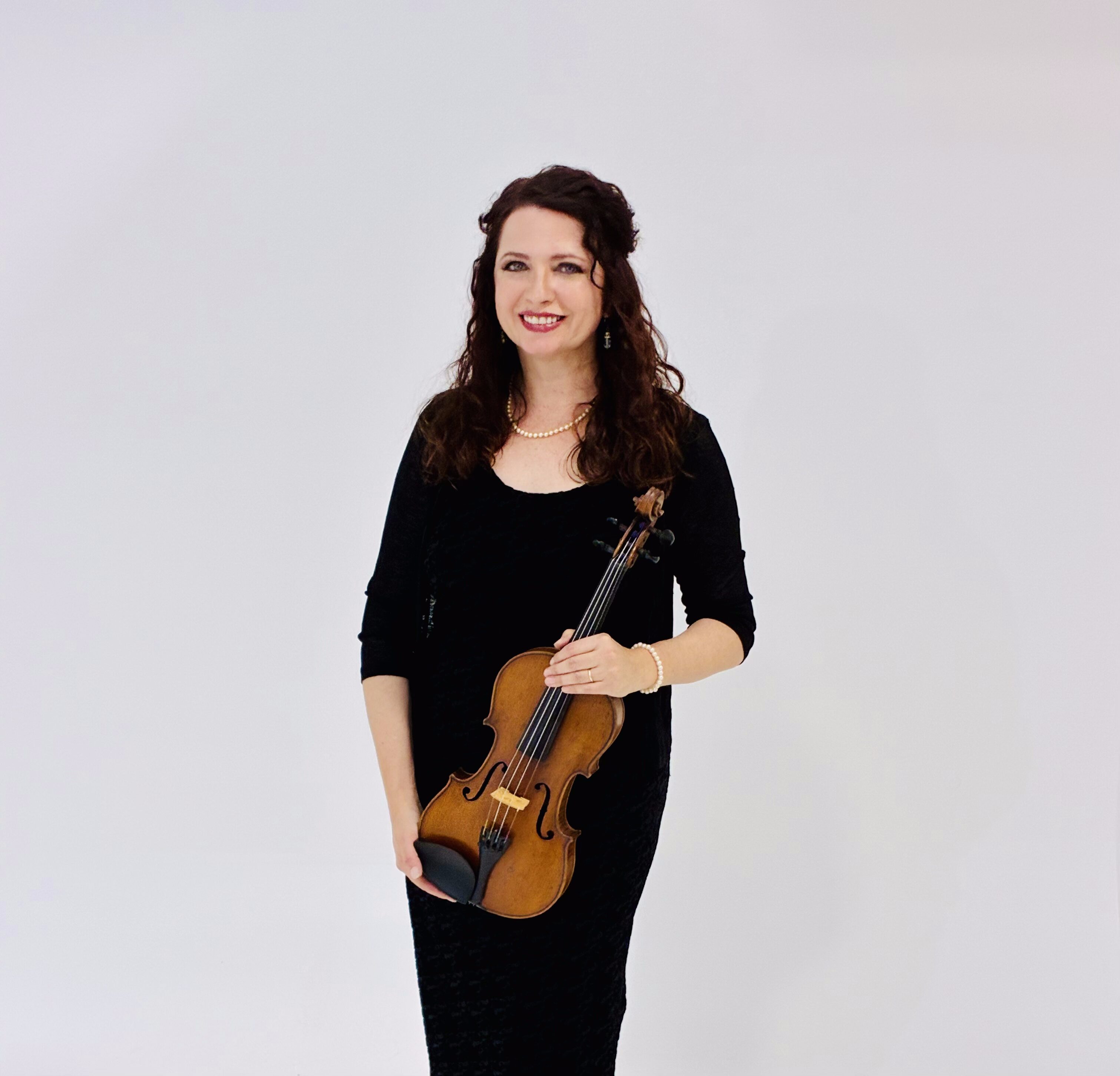 Woman in black holding a violin and bow, smiling against a white background.
